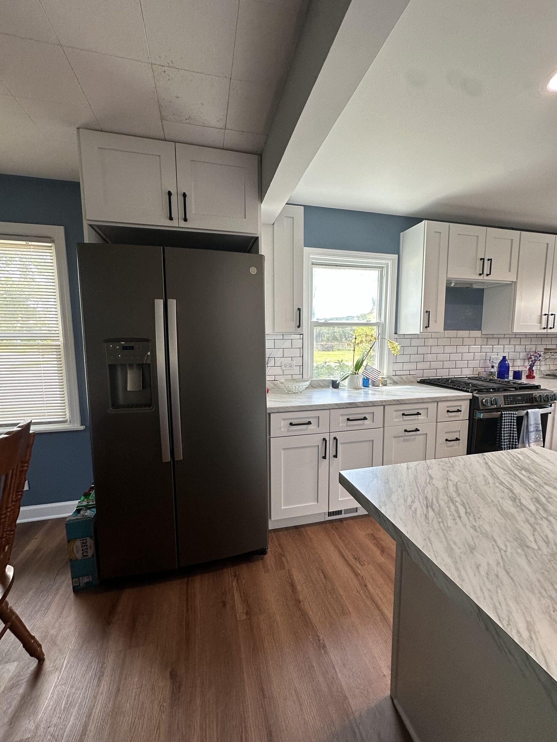 Mundelein kitchen with white cabinetry, black refrigerator, island, and wood flooring